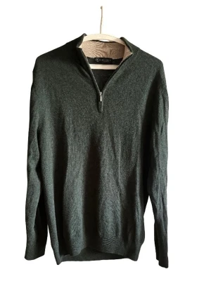 Mörkgrön stickad tröja med halvzip - Mörkgrön stickad tröja med halv dragkedja och hög krage. Tröjan har lång ärm och ribbstickade muddar vid ärmslut och nederkant. Perfekt för lager-på-lager och stilren look. Merino ullll