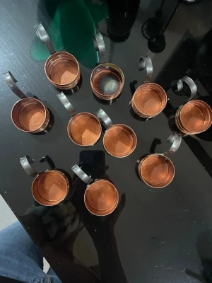 10 små koppar i koppar med metallhandtag - Säljer ett set med 10 små koppar i kopparfärgat metallmaterial. Kopparna har rund form och robusta, svarta metallhandtag med böjd design. Perfekta för dekoration eller servering av små drycker. Snygg retrostil som sticker ut på bordet.