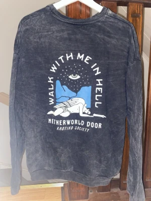 Svart sweatshirt med tryck från Kaotiko BCN - Cool svart sweatshirt från Kaotiko BCN med tryck på ryggen: 'Walk with me in hell', motiv av en fallande ängel, blå bakgrund och öga ovanför. Tröjan har rund hals och avslappnad passform. Perfekt för dig som gillar streetwear och unika prints. Storlek xs