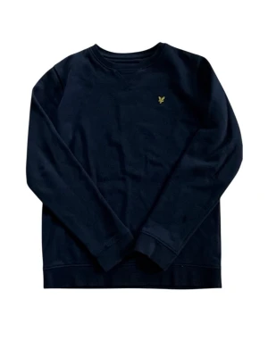 Mörkblå sweatshirt från Lyle & Scott - Mörkblå sweatshirt med rund hals från Lyle & Scott. Tröjan har ett litet gult logomärke broderat på bröstet och är tillverkad i mjukt bomullsmaterial. Klassisk passform med långa ärmar och ribbade muddar.