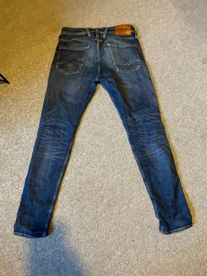 Mörkblå slim fit jeans från Replay - Säljer ett par mörkblå slim fit jeans från Replay med klassiska bakfickor och snygga kontrastsömmar. Jeansen har en skinnpatch med Replay-logga bak i midjan och är tillverkade i mjukt denimtyg med lätt tvättad look. Anbass w30 L32