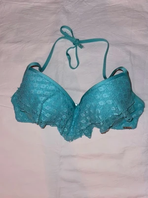 Bikini - Snygg turkos bikiniöverdel med vadderade kupor och volangdetaljer i spets. Knytband i nacken för justerbar passform. Perfekt för strandhäng och poolparty. Materialet känns mjukt och bekvämt mot huden.saknar tyvärr lapp men skulle säga att den passar 70/75 