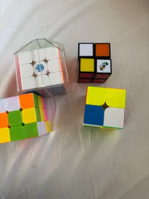 Fyra olika Rubiks kuber - Säljer fyra olika Rubiks kuber i olika färger och former. En kub är i genomskinlig förpackning, en är klassisk 2x2 med färgade sidor, en har neonfärger och en har två färger per sida. Perfekt för dig som gillar hjärngympa och pussel.
