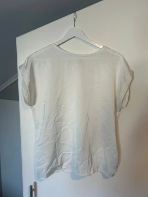 Vit enkel blus i luftig modell - Säljer en vit blus med rund hals och korta ärmar. Blusen har en lös passform och är tillverkad i ett tunt, luftigt material som passar perfekt till varma dagar. Enkel och stilren design utan mönster eller detaljer.