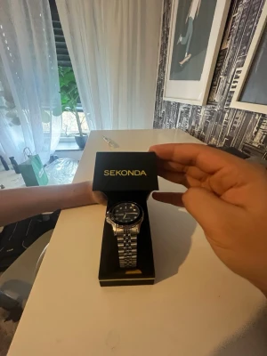 Sekonda silverfärgad klocka - Stilren klocka från Sekonda med silverfärgad länkarmband i metall och svart urtavla. Klassisk rund form och tydliga markeringar på urtavlan. Perfekt accessoar för dig som vill ha en tidlös look , inte använd!