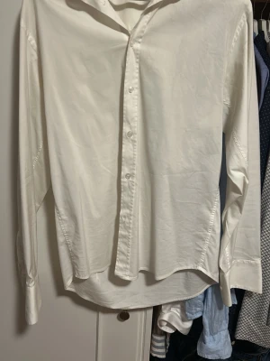 Vit klassisk skjorta i bomull  - Säljer en stilren vit skjorta med lång ärm och knappar framtill. Skjortan har klassisk krage och är tillverkad i mjuk bomull, perfekt för en clean och enkel look. Passar till allt från jeans till kostymbyxor.