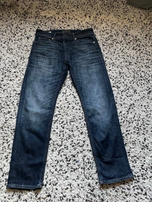 Jeans 30/30 - Snygga mörkblå jeans med raka ben och diskreta slitningar framtill. Klassisk femficksmodell med knappgylf och läderpatch bak i midjan. Jeansen har en tvättad look som ger en avslappnad stil. Perfekta till vardagslooken och passar till det mesta.