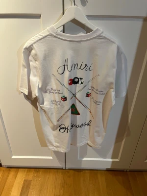 Vit Amiri t-shirt med biljardtryck - Snygg vit t-shirt från Amiri med coolt biljardinspirerat tryck på både fram- och baksidan. Klassisk passform med rund hals och korta ärmar. Perfekt för dig som gillar streetwear och vill sticka ut med en unik design. Storlek M men passar som L 