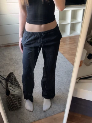 Svarta linnebyxor med låg midja - Snygga svarta linnebyxor med avslappnad passform och resår i midjan. Byxorna har raka ben och är tillverkade i ett lätt och luftigt linnematerial, perfekta för en chill och stilren look.