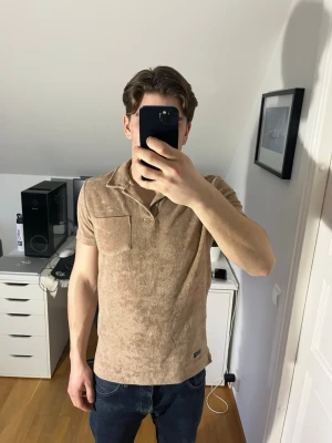 Beige frotté kortärmad topp Robbie Moor - Säljer en beige skjorta från Robbie Moor i bomull men känns och ser ut som frotté. Skjortan har korta ärmar, bröstficka och klassisk krage. Hör gärna av dig vid frågor!