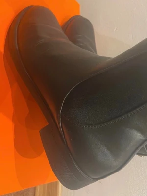 Svarta Chelsea boots i skinn - Stilrena svarta Chelsea boots i slätt skinn med klassiska resårpaneler på sidorna och rundad tå. Sitter på låg sula och har dragflik baktill för enkel påtagning. Perfekta för en trendig och tidlös look.