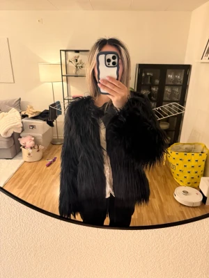 Svart pälsjacka - Säljer en svart pälsjacka med rak passform och rund halsringning. Jackan har ett coolt och trendigt utseende som passar perfekt för kalla vinterdagar. Materialet är syntetpäls och jackan är utan synliga detaljer eller mönster. Storlek Xl skulle säga mer som xs-S