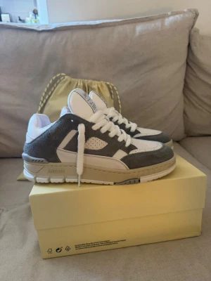 Axel Arigato gråvita sneakers - Snygga sneakers från Axel Arigato i grått och vitt. Skorna har en chunky sula, perforerade detaljer på sidan och ovandel i mocka och läder. Klassisk låg modell med vita skosnören och diskret logga på sidan. Perfekta för dig som gillar stilrena och trendiga sneakers.  HELT NYA OANVÄNDA. Säljs PGA de inte kommer till användning. 