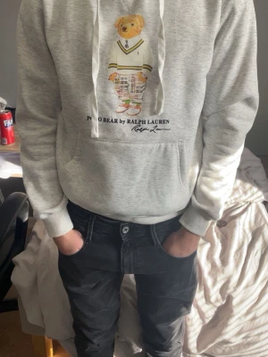 Grå hoodie Polo Bear Ralph Lauren - Snygg grå hoodie från Ralph Lauren med Polo Bear-tryck på bröstet. Klassisk känguruficka och huva med dragsko. Mjuk bomullskänsla och avslappnad passform, perfekt till jeans eller joggers. PRIS GÅR ATT DISKUTERAS!!!