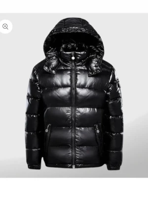 Svart pufferjacka - En svart pufferjacka med dragkedja längs luvan, knappar på både luvan och längst ut på ärmarna. Jackan har en svart logga på ena armen. Passformen är mer baggy, passar både S/M. Annars är den knappt använd och i jätte fint skick. Har aldrig fryst i denna jacka❣️