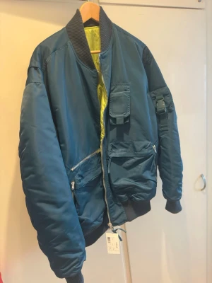 Unik jacka ifrån Helmut Lang.  - Helmut Lang/ Nylon Bomber. Svårt att få tag i.  Snygg mörkblå bomberjacka med flera praktiska fickor och svart ribbstickad krage, ärmslut och midja. Jackan har en cool gul insida och dragkedja framtill. Perfekt för dig som vill ha en streetig och trendig look. Stor i storlek. 