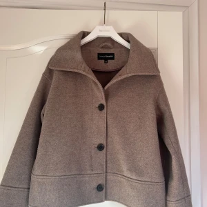 Beige jacka från KappAhl - Snygg beige jacka från KappAhl  med stora knappar framtill och bred krage. Jackan har en rak, något boxig passform och är perfekt för kyligare dagar. Enkel och stilren design som passar till det mesta. Två fickor på sidan!