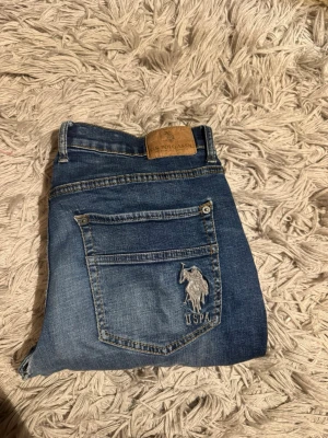 U.S. Polo Assn. Jeans - Snygga blå jeans från U.S. Polo Assn. med klassisk femficksdesign och broderad logga på bakfickan. Jeansen har en rak passform och slitningar för en cool, avslappnad look. Storleken är W31 L34.Pris kan diskuteras vid snabb affär! Bara att höra av sig vid minsta fundering.