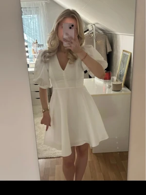 Studentklänning- kortärmad  - Säljer en vit kortklänning med v-ringning och puffiga kortärmar, perfekt till studenten!!. Klänningen har en markerad midja och ett lätt utsvängt kjolparti som ger en feminin siluett. Perfekt för sommarens alla tillfällen. Materialet känns mjukt och lätt. Aldrig använd!!! (Pris kan diskuteras)