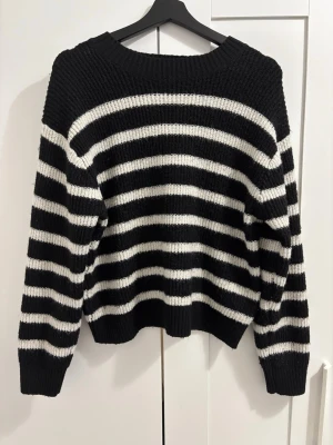 Randig stickad tröja - Säljer en svart stickad tröja med vita horisontella ränder. Tröjan har rund halsringning, långa ärmar och ribbade muddar vid ärmslut och nederkant. Supersnyggt med ett par jeans eller en kjol! Perfekt för dig som gillar klassiska mönster och vill ha en mysig, oversized look. Skriv gärna innan ni köper❤️