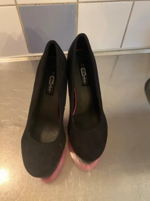 Svarta pumps med rosa klack från Din Sko - Säljer ett par snygga pumps från Din Sko i storlek 35. Skorna är svarta med mockaliknande material och har en cool rosa platå och klack som sticker ut. Rund tå och klassisk siluett gör dem perfekta för dig som vill ha något extra.