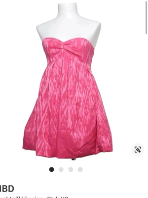 Rosa axelbandslös kortklänning - Snygg rosa axelbandslös kortklänning med mönstrad yta och lätt vidd i kjolen. Klänningen har en twistad detalj vid bysten och är perfekt för dig som vill sticka ut. Materialet känns lätt och passar bra till varmare dagar.