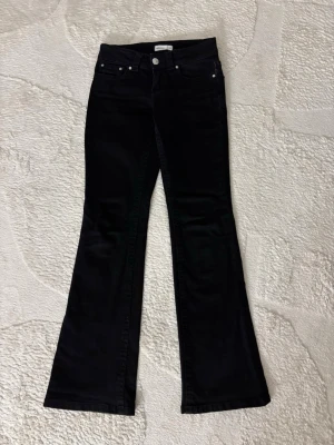 Svarta bootcut jeans från Gina Tricot - Snygga svarta bootcut jeans från Gina Tricot med klassisk femficksdesign och silverfärgade knappar. Jeansen har utsvängda ben och normal midja, perfekta för en trendig look. Tillverkade i stretchigt denimtyg för extra komfort.