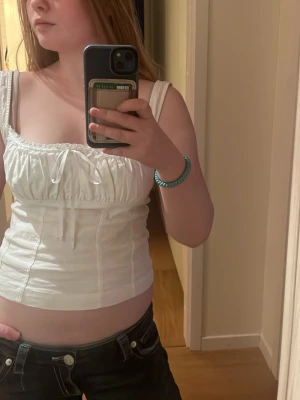 Vit korsett-topp med snörning - Snygg vit korsett-topp med smala axelband och söt snörningsdetalj framtill. Toppen har en figurnära passform och markerad midja.Perfekt att styla med jeans eller kjol för en cool look.