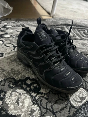 Nike Air VaporMax Plus svarta sneakers - Svarta Nike Air VaporMax Plus sneakers med en chunky sula och ikoniska vågformade detaljer på sidorna. Ovandelen är i textil och syntet, med snörning och dragflik bak. VaporMax-dämpning i sulan för extra komfort. Snygg och sportig look.