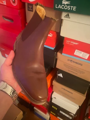 Bruna Chelsea boots i läder - Snygga bruna Chelsea boots i slätt läder med klassiska resårpaneler på sidorna och dragflik bak. Skorna har en låg klack och rundad tå, perfekt för en stilren look. Passar till jeans eller chinos för en clean outfit.