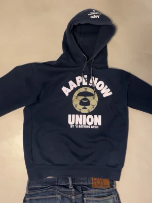 Mörkblå hoodie från AAPE BY A BATHING APE - Säljer denna väldigt snygga AAPE hoodien, som är skapad utav Bape. Storlek S. Skickas i original förpackning. Rätt unik och sällsynt, så missa inte chansen. Skriv vid frågor eller funderingar. Väldigt snabba svar 🙂