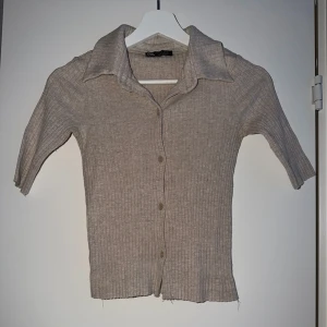 Beige ribbad kofta med krage - Säljer en beige ribbad kofta från Zara Knit med korta ärmar och klassisk krage. Koftan har knäppning framtill med fem knappar och är tillverkad i ett mjukt, stretchigt material. Perfekt för lager på lager och enkel att styla till olika outfits.