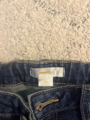 Blå bootcut jeans från Gina Tricot - Snygga blå bootcut jeans från Gina Tricot med klassisk femficksmodell och kontrastsömmar. Jeansen har en lätt utsvängd passform nedtill och är tillverkade i ett mjukt denimtyg som ger en bekväm känsla. Perfekta för en trendig vardagslook.