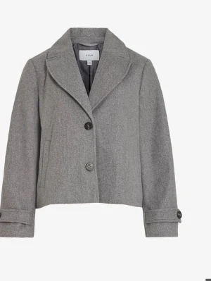 Grå kort kappa från Vila - Stilren grå kappa från Vila med kort, boxig passform och klassisk krage. Kappan har två knappar framtill, diskreta sidfickor och dekorativa knappar vid ärmsluten. Perfekt för dig som gillar minimalistisk och trendig stil.