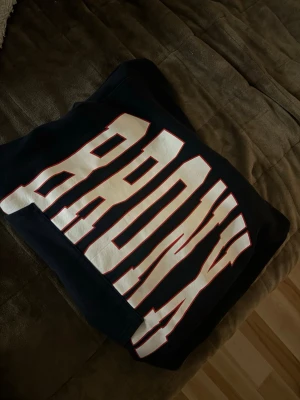 Mörkblå hoodie med BRONX-tryck - Cool svart hoodie med stor vit text 'BRONX' över bröstet. Oversized passform och klassisk huva. Ribbat vid ärmar och midja. Aldrig använd