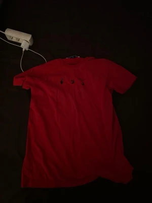 Röd t-shirt med svart tryck - Cool röd t-shirt med svart grafiskt tryck på ryggen och små detaljer framtill. T-shirten har rund hals och korta ärmar, perfekt för en avslappnad stil. Materialet känns mjukt och skönt mot huden.