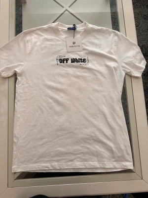 Vit t-shirt med tryck - Säljer en vit t-shirt med svart logga och grafiskt tryck fram och bak. T-shirten har rund hals, korta ärmar och är gjord i mjuk bomull. Baksidan har ett stort färgglatt motiv och textdetaljer. Perfekt för dig som gillar streetwear och statement-plagg. Storlek Xl men skulle säga att den passar en L också 