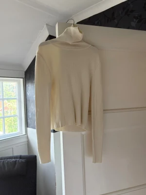 Beige ribbad polotröja 💗 - Säljer en stilren beige stickad polotröja med ribbad struktur och långa ärmar. Tröjan har en hög polokrage och är tillverkad i ett mjukt, stretchigt material som sitter snyggt på kroppen. Perfekt för lager på lager och enkel att matcha. 💕💕🍓