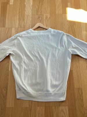 Beige/Vit sweatshirt från Polo Ralph Lauren - Vit sweatshirt från Polo Ralph Lauren med rund hals och broderad marinblå logga på bröstet. Tröjan har långa ärmar, ribbade muddar och är gjord i mjukt bomullsmaterial. Enkel och stilren design som funkar till det mesta.