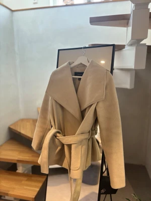 Beige kappa från Vero Moda - Beige kappa från Vero Moda med bred krage och knytskärp i midjan. Kappan har en klassisk, rak passform. ( kan tänkas gå ner i pris ) 