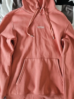 Rosa hoodie från H&M Artisan XS - Säljer en snygg rosa hoodie från H&M med trycket 'Artisan The Creative Collective' på bröstet. Hoodien har huva med dragsko, stor magficka och ribbade muddar. Perfekt för chill dagar och streetwear vibes.