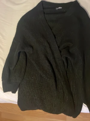 Svart kofta från H&M Divided - Mysig svart kofta från H&M Divided i storlek L. Koftan är stickad med lös passform och har långa ärmar samt bred ribbad kant framtill. Perfekt att slänga på sig när det är kyligt ute.