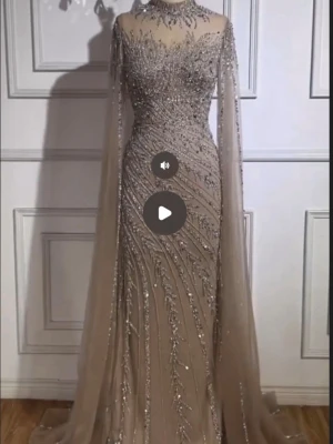 Champagnefärgad långklänning med glitter - Elegant maxi klänning i champagnefärg med glittriga paljettdetaljer och transparent mesh upptill. Klänningen har lång ärm med cape-liknande fall och figurnära passform. Perfekt för dig som vill sticka ut på bal eller fest. Klänningen är tillverkad i Tyskland och endast använder några timmar. Tillkommer en topp under ifall man vill ha de. 