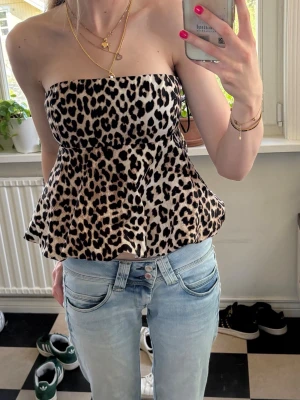 Leopardmönstrad axelbandslös topp - Säljer en snygg axelbandslös topp med leopardmönster och utsvängd passform. Toppen har bandeau-modell och är perfekt för dig som vill sticka ut. Materialet känns mjukt och följsamt, och färgerna går i beige, svart och brunt. Har aldrig använt tröjan så prislappen är kvar!💕💕