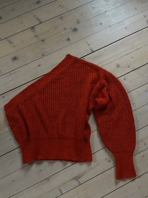 Röd one shoulder stickad tröja - Trendig röd stickad tröja med one shoulder-design och bred ribbad mudd. Tröjan har en avslappnad passform och är tillverkad i ett mjukt, grovt stickat material. Perfekt för dig som vill sticka ut med en unik och cool look. Röd/orange färg. Aldrig använd. Perfekt till en sommarkväll. Pris kan diskuteras!🥰