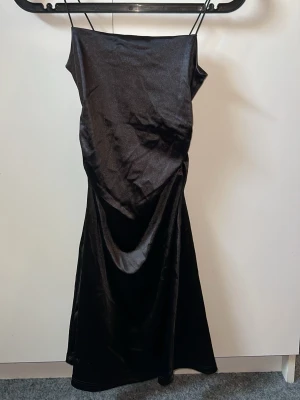 Svart långklänning från H&M Divided - Elegant svart klänning från H&M Divided med tunna axelband och slät, glansig yta. Aldrig använd med lappen kvar 