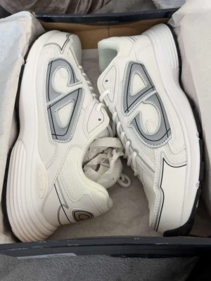 Axel Arigato vita sneakers med grå detaljer - Helt nya för stora för mig Snygga vita sneakers från Axel Arigato med grå och svarta detaljer. Skorna har en chunky sula, meshpaneler och coola grafiska linjer på sidorna. Perfekta för dig som gillar stilrena men ändå unika sneakers.
