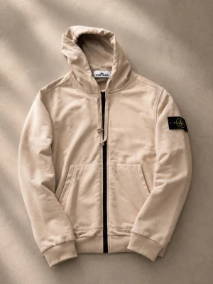 Beige hoodie från Stone Island - Snygg beige hoodie från Stone Island med dragkedja framtill och klassisk patch på vänster ärm. Tillverkad i mjuk bomull, har två fickor fram och ribbade muddar. Perfekt för en avslappnad streetwear-look.