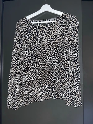 Leopardmönstrad blus med vida ärmar - Snygg blus med leopardmönster i svart och beige. Blusen har rund halsringning och långa, lite utsvängda ärmar. Tillverkad i lätt och luftigt viscose  som ger en avslappnad men trendig look. Perfekt för dig som vill sticka ut med ett djurmönster.