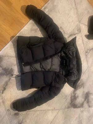 Svart pufferjacka med huva - Säljer en svart pufferjacka från zalando med stor huva och dragkedja framtill. Jackan har en boxig passform och är vadderad för extra värme. Perfekt för kalla vinterdagar och har justerbar dragsko nedtill för bättre passform.